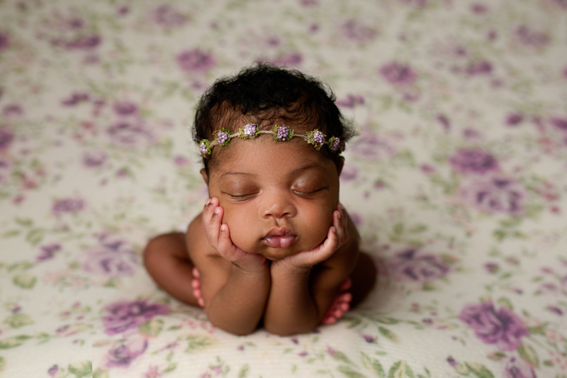 Newborn Photographer, a baby girl sleeps propped on her arms on a floral bedsheet