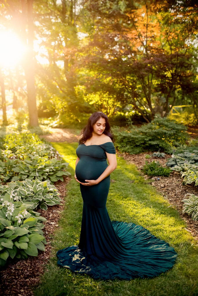 Maternity Photographer, a woman holds her belly in the forest at golden hour, she is all dressed up