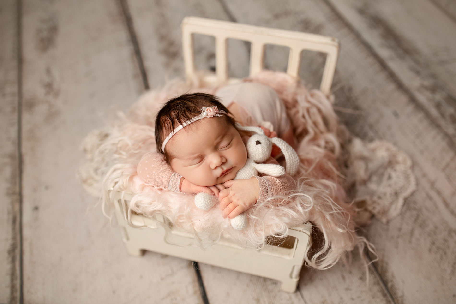 Newborn Photographer, a baby lays sleeping a small wooden dollhouse baby bed,