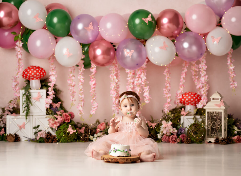 Baby girl eats a floral cake for her cake smash with mushrooms and butterflies with balloons