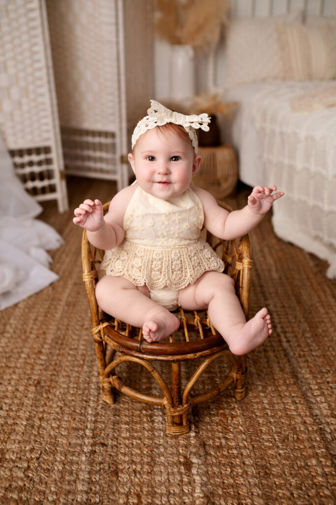 Baby girl smiles in a small children's chair while posing in a prop bedroom