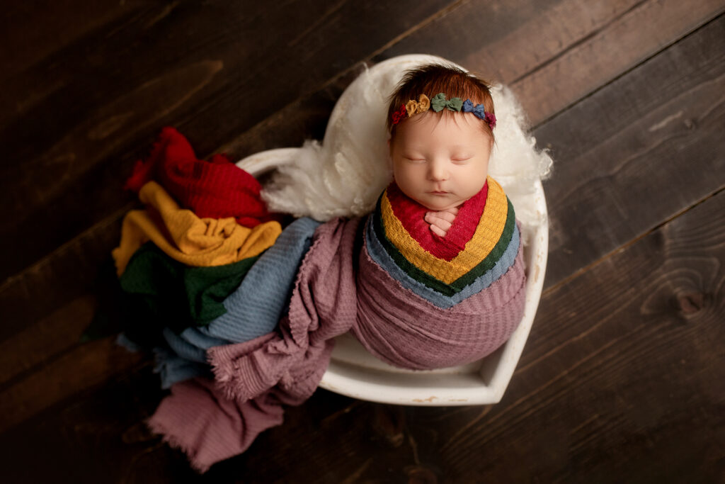 Newborn baby girl sleeps in a wooden heart with rainbows