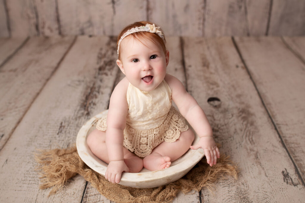 Baby girl smiles in a bowl while wearing a boho cream romper