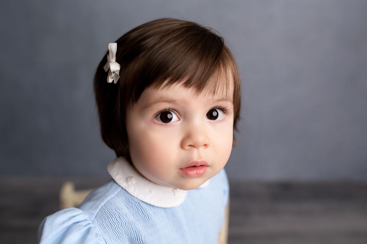Toddler girl with large eyes wears a blue dress for milestone portraits