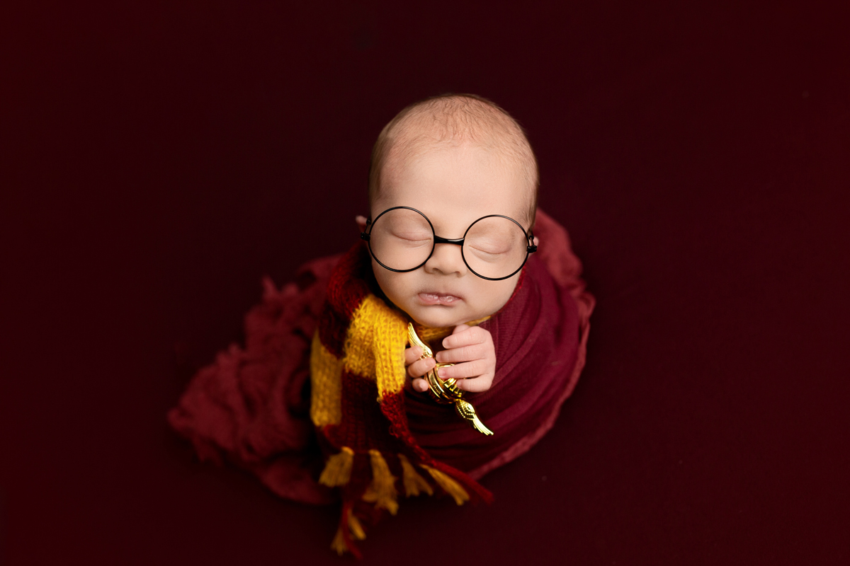 Newborn baby boy swaddled in red wearing glasses and a scarf