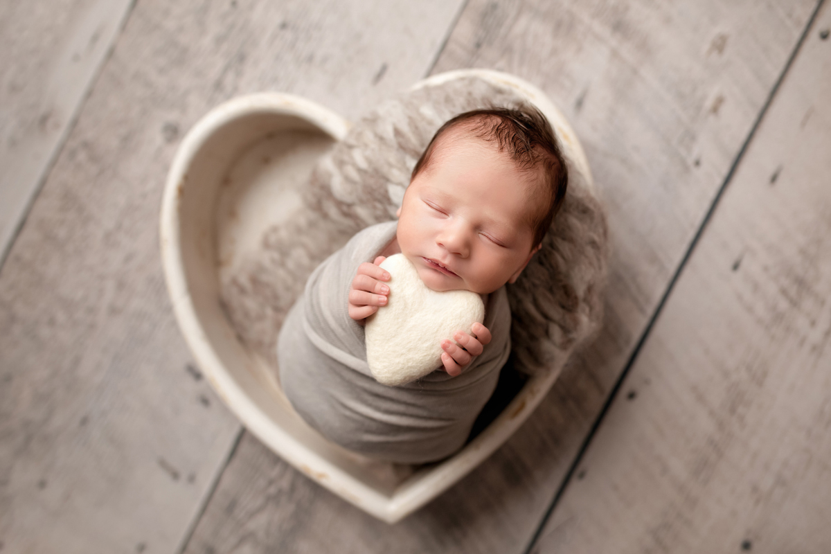 Newborn Photography, a newborn baby boy sleeps in a wooden heart holding a heart in his hands