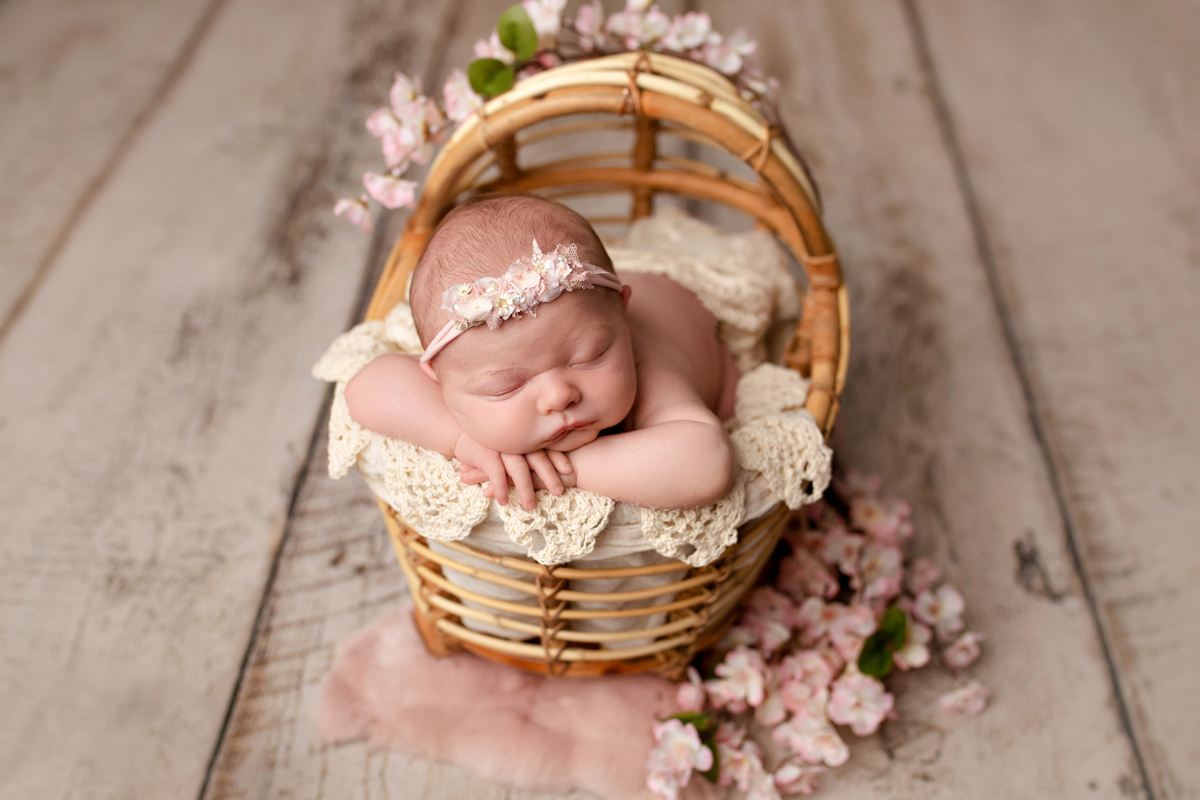 Baby girl sleeps in a Bamboo cradle with baby pink flowers and lace