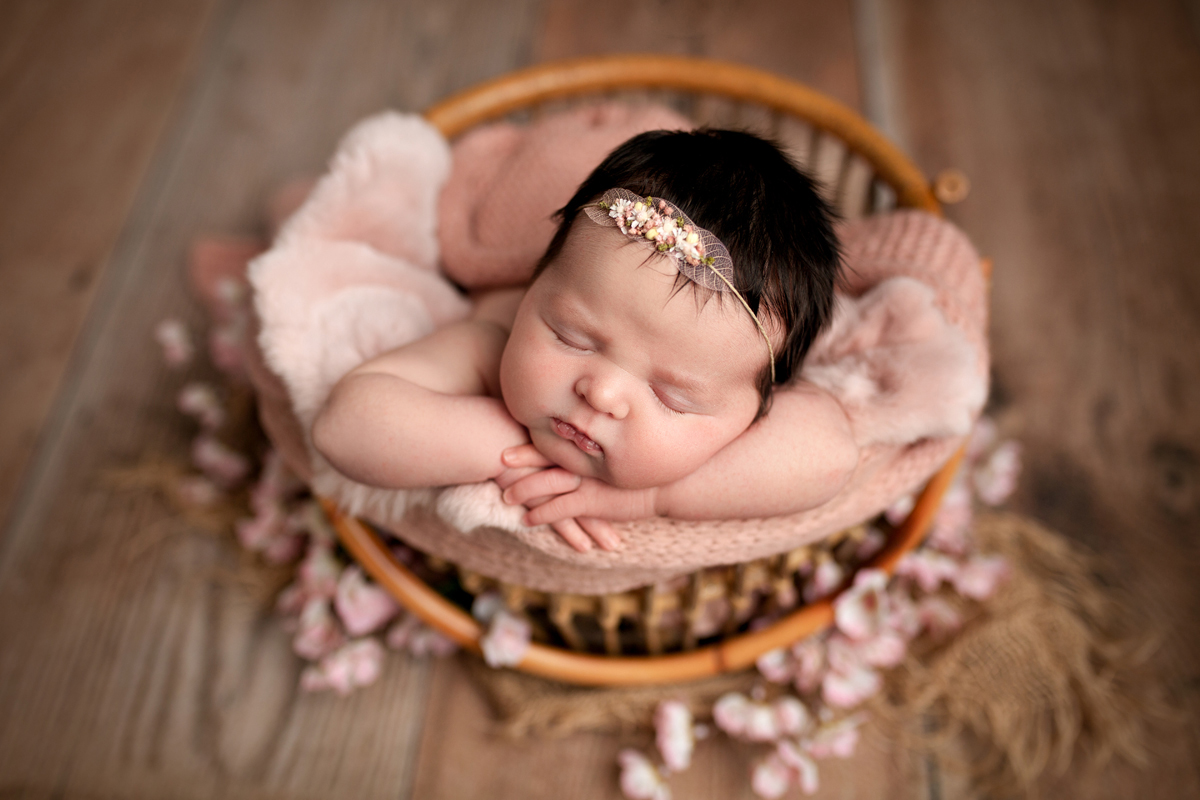 Newborn Baby Girl Sleeping in a Basket with Pink Flowers and Leaf Headband