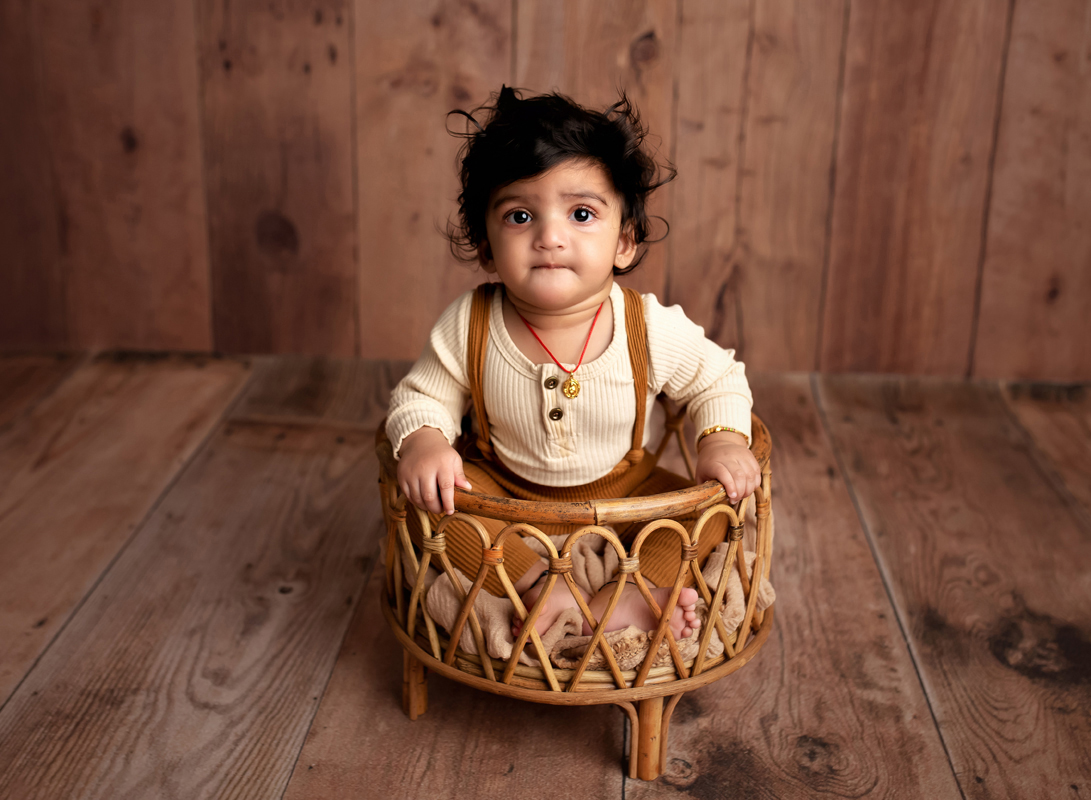 Baby Boy with curly hair sits in a boho basket on a wooden background