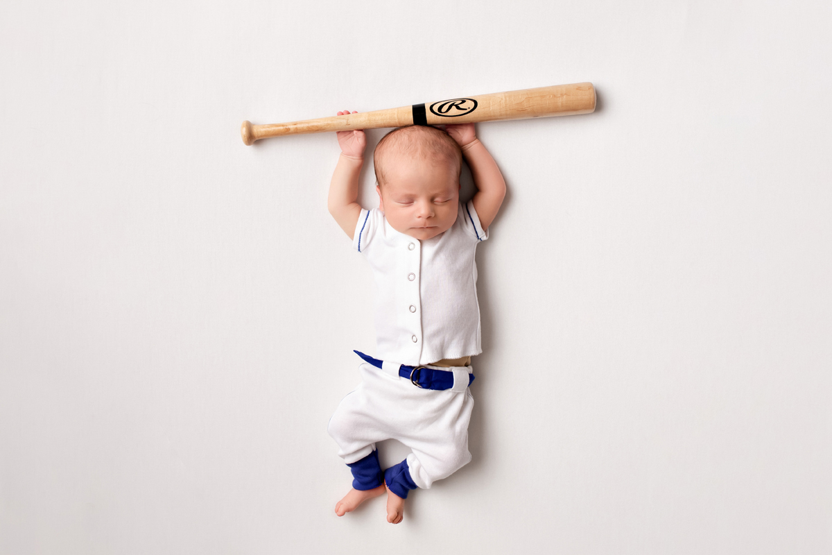 Newborn Baby Boy holds baseball bat wearing a baseball uniform