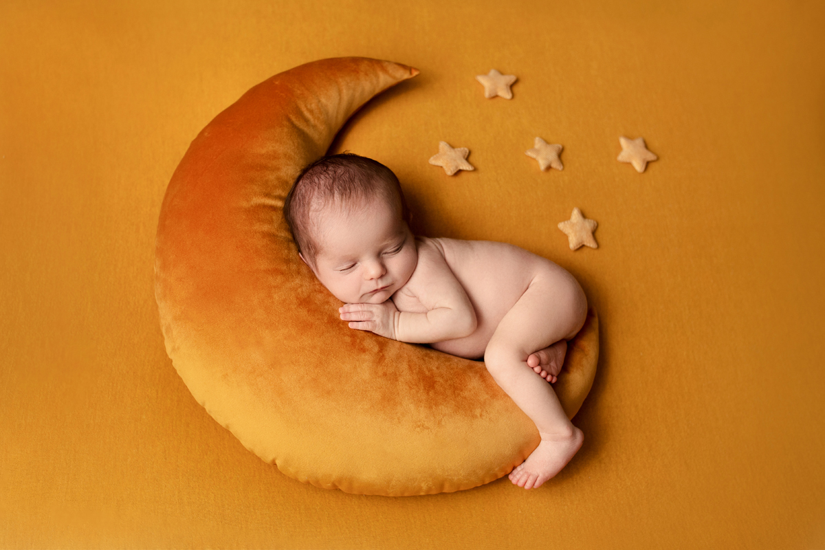 Baby boy sleeps peacefully on a yellow moon with yellow stars around him