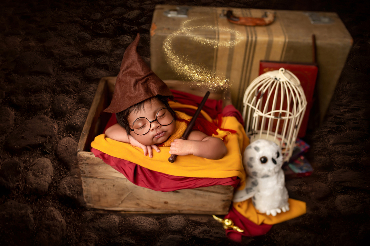 Baby Boy sleeps in a wooden crate with cobblestone floor wearing glasses and holds a magic wand