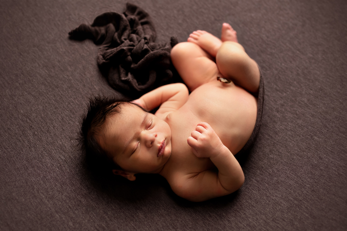 Newborn boy is posed naturally on a gray background