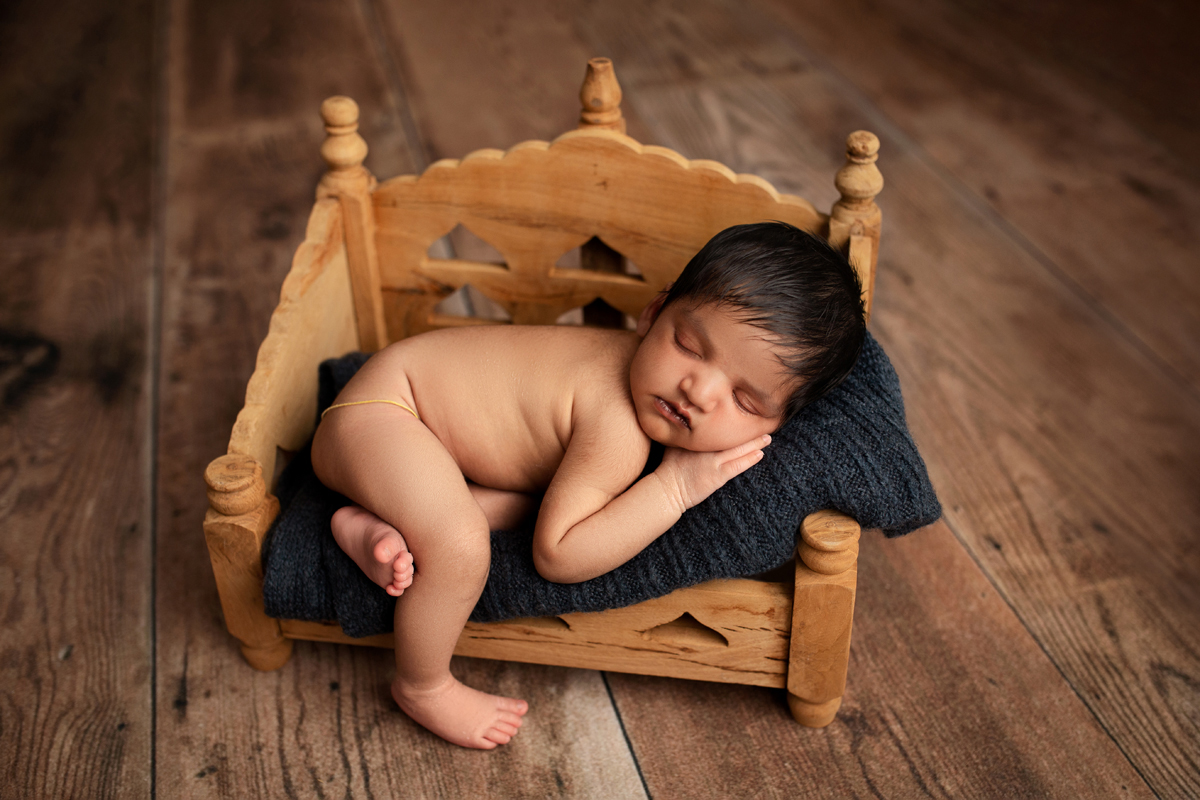 Baby boy sleeps on a wooden bed on a navy blue blanket