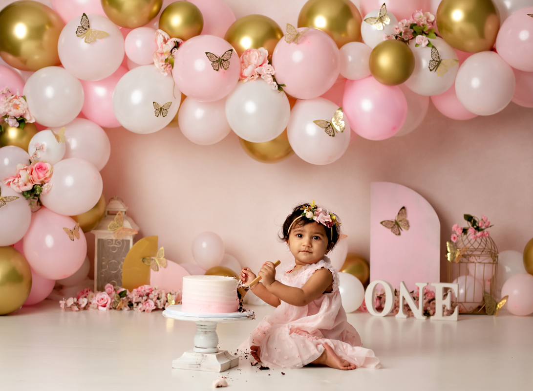 Baby Girl eats cake during her butterfly cake smash session with gold balloons