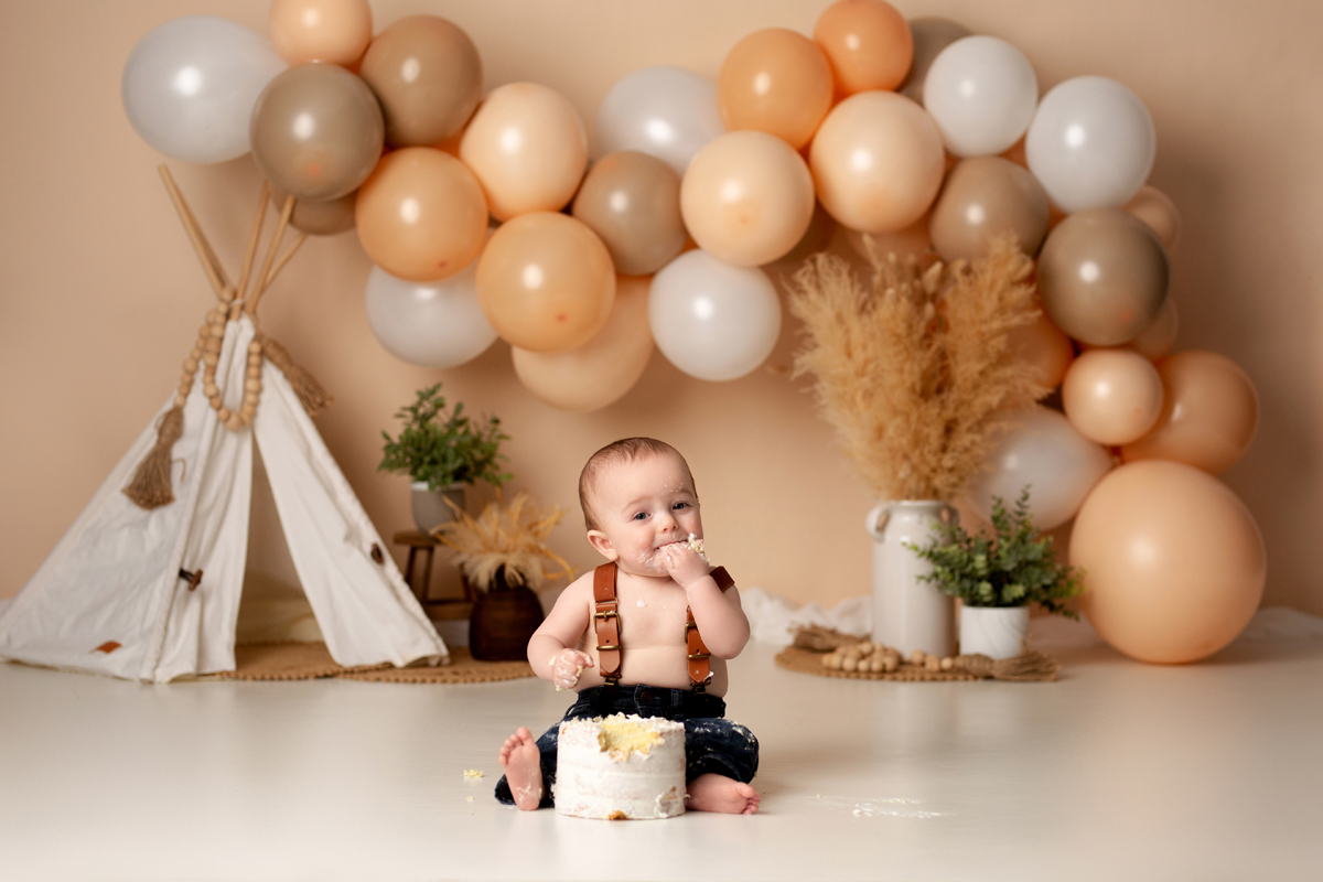 Baby boy celebrates first birthday with balloons and is decorated with a boho background
