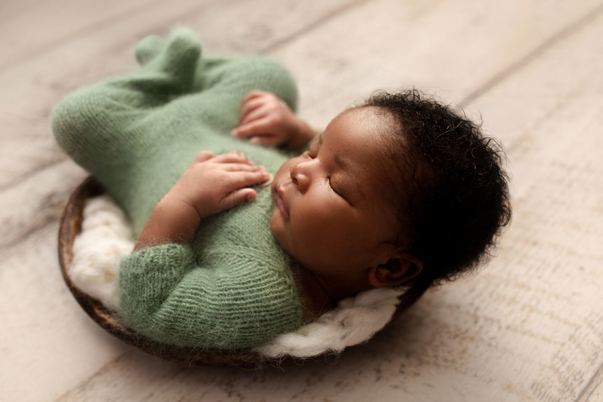 Newborn baby boy sleeps in a bowl wearing a green outfit