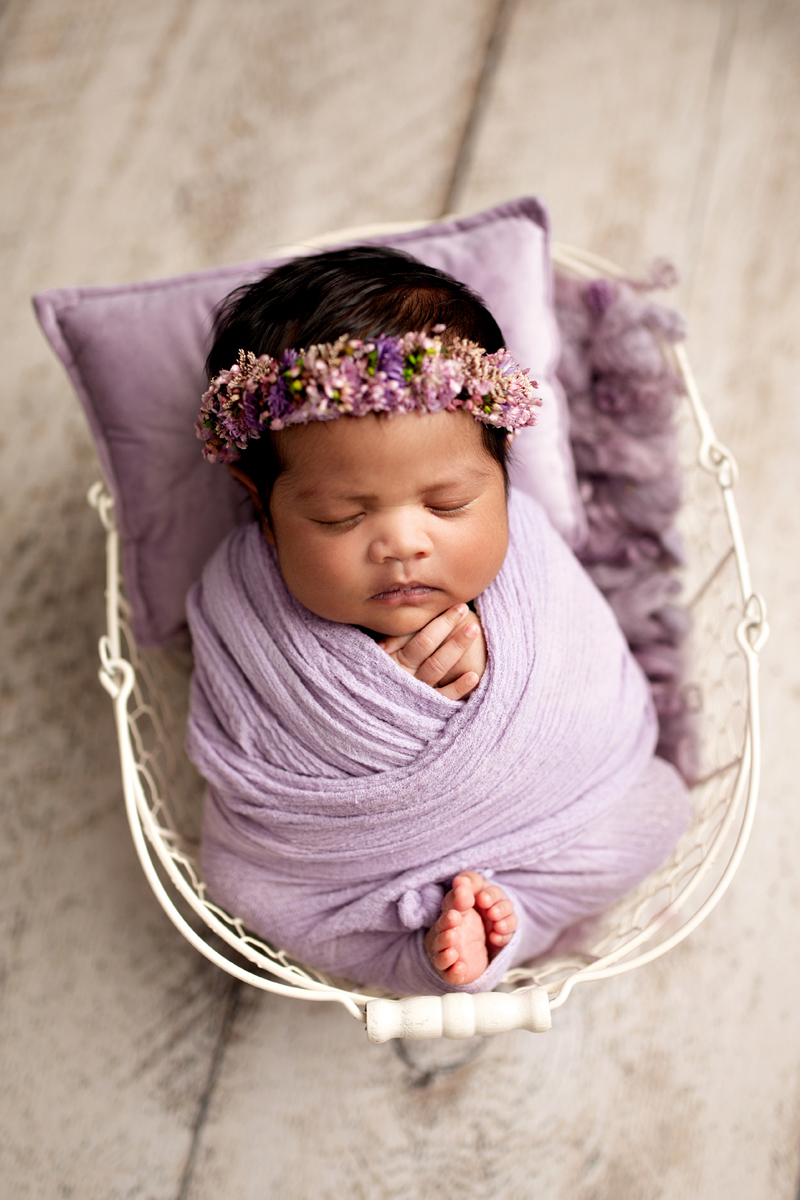 Newborn baby girl swaddled in a purple wrap with baby toes in a white basket