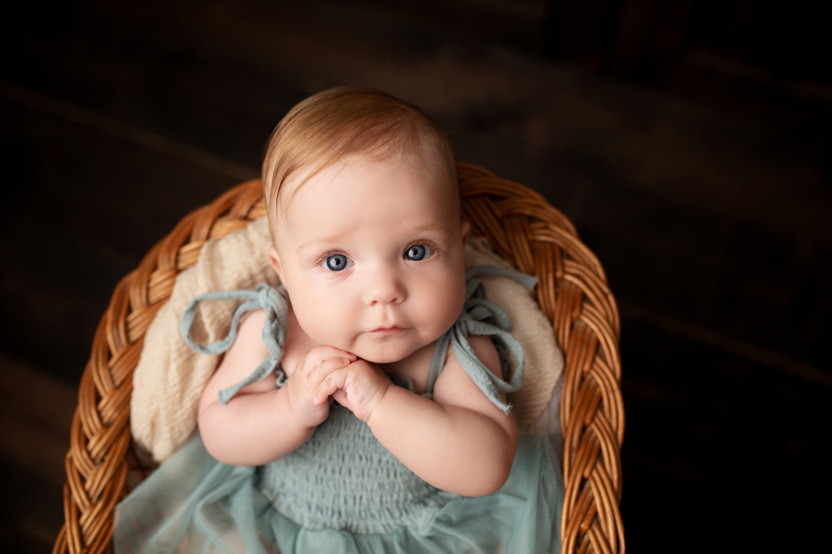 Baby girl with blond hair sits in a chair wearing a green dress