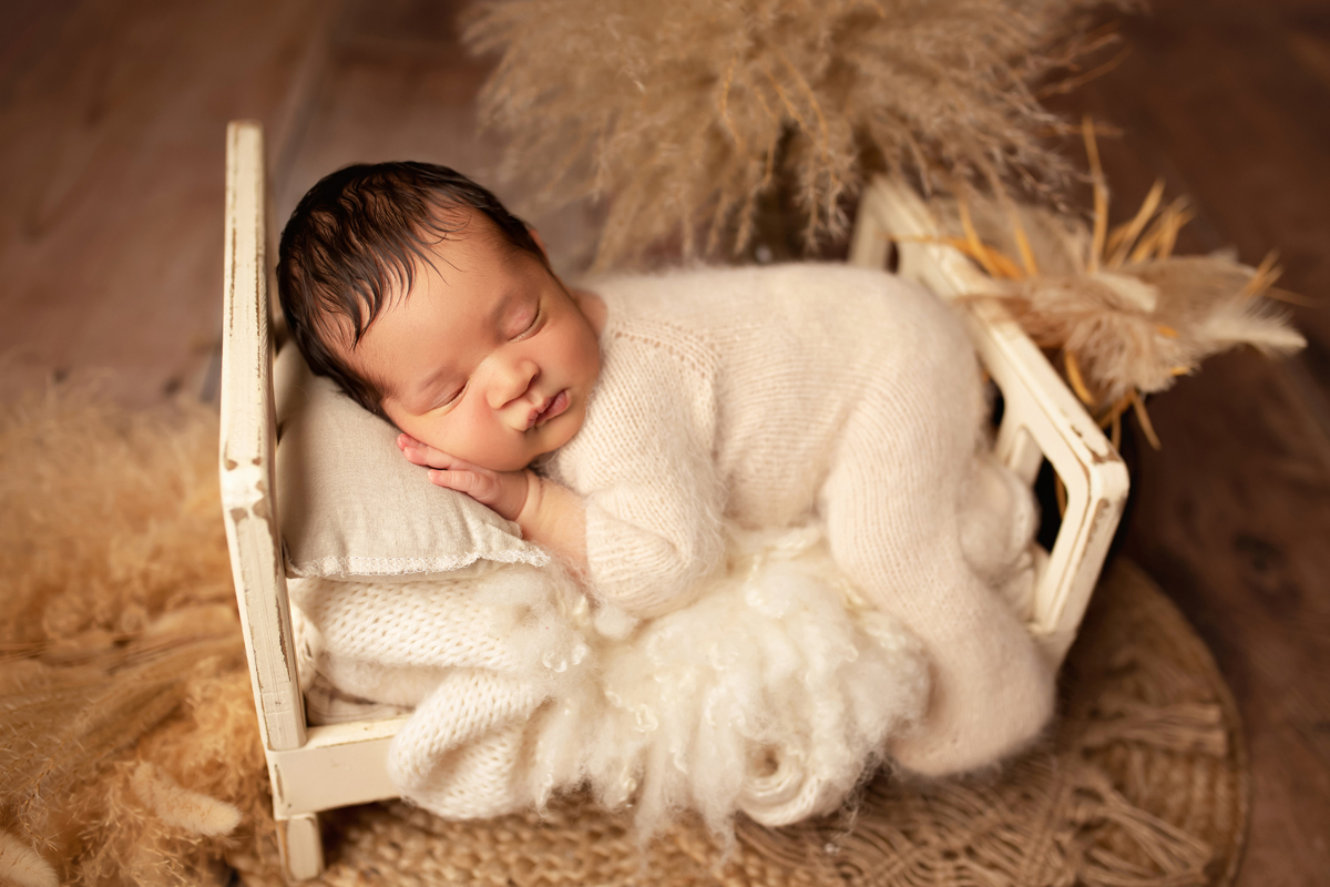 Newborn boy sleeps in a wooden baby bed on a pillow with boho grass