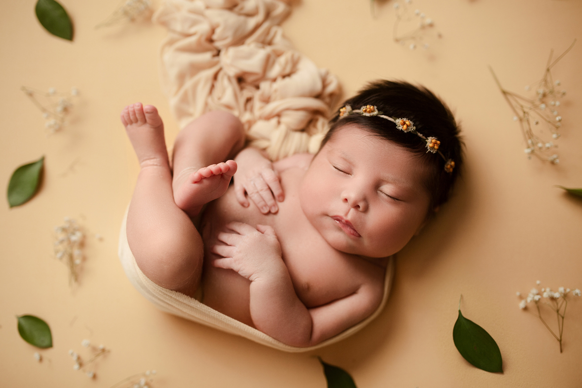 Newborn baby girl sleeps on a yellow blanket surrounded by flowers