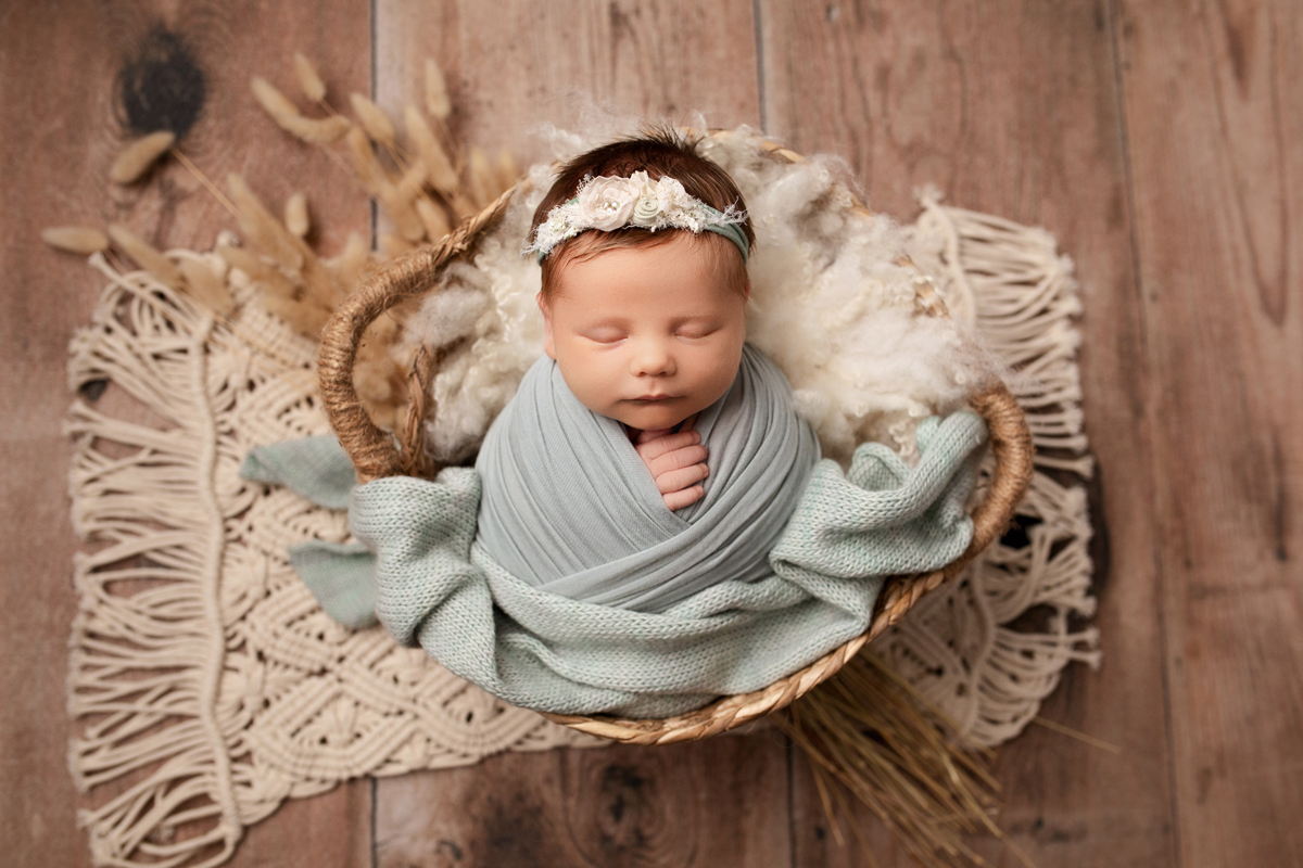 Newborn Baby Girl Swaddled in Boho Basket in Sage Green on Boho Rug with Wheatgrass