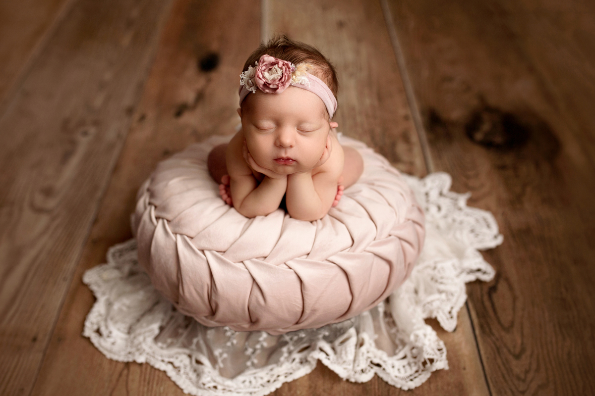 Baby in Froggy Pose with Pink Headband on Tufted Circle Pillow and Wood Floor