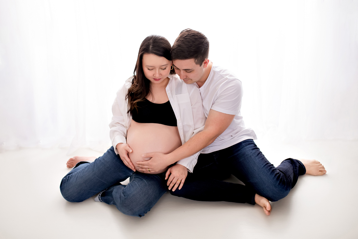Couple on Floor in Front of White Backdrop, Mom is Expecting Twins
